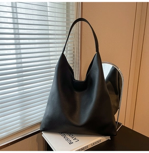 Detail of minimalist black pebbled leather tote bag placed on white books in natural light