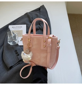 Rosa glänzende Beuteltasche mit abnehmbarem Gurt und weißem Plüschanhänger auf Anzug-Hintergrund