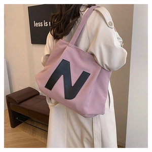 Detail of a pink canvas tote bag with a black letter N print, showing large capacity style