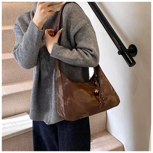 Detail of dark brown glossy shoulder bag with a gold sphere charm and woven lanyard