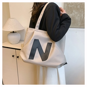 Close-up of a large beige canvas tote bag with a bold black N logo worn by a model