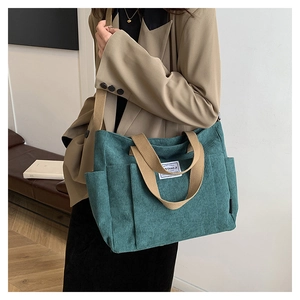 Detail of teal corduroy tote bag showing ribbed texture and side pockets on a model