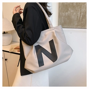 Detail of beige canvas tote bag featuring a leather N patch and large interior capacity