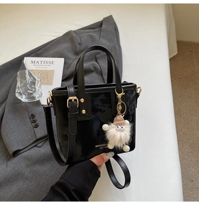 Detail einer glänzenden schwarzen Lackleder-Beuteltasche mit weißem Plüsch-Anhänger