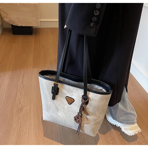 Détail d'un sac cabas gris avec texture mate, logo triangulaire et accessoire de corde