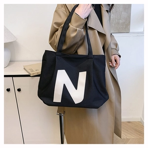 Close-up of black canvas tote bag with white N logo and wide shoulder strap detail