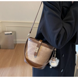 Close-up of vintage brown leather bucket bag featuring a gold metal buckle and plush charm