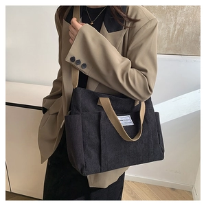 Close-up of black corduroy tote bag featuring brown straps and brand label detail