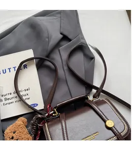 Macro detail of dark brown leather handbag with gold bead trim and plush bear charm