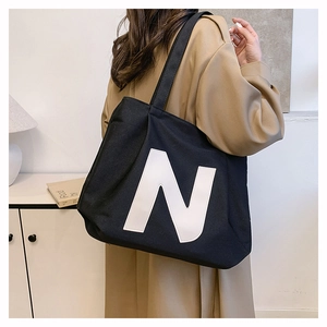 Close-up of a black canvas tote bag with a large white N logo on a model in a trench coat