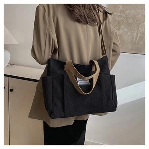On-body view of a black corduroy tote bag with brown straps and side pocket detail