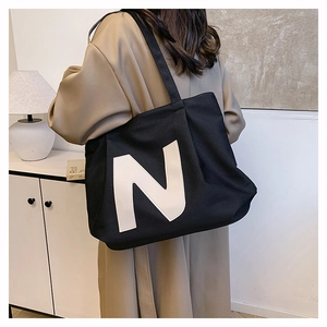 Detail shot of a large black canvas tote bag with a white N logo worn on the shoulder
