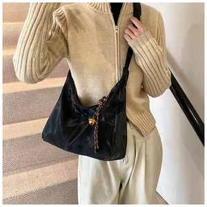 Detail of black satin crescent shoulder bag featuring gold bell and woven rope pendant