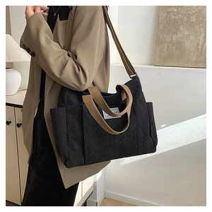 Detail of black corduroy tote bag showing side pocket, white label, and khaki straps