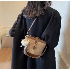 Close-up of retro bucket bag with brown leather and canvas, featuring a plush charm