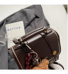 Close-up of vintage brown leather bag with gold rivets and cute plush charm on grey blazer