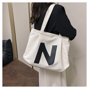 Detail of large beige canvas tote bag featuring black stitched N letter and shoulder straps