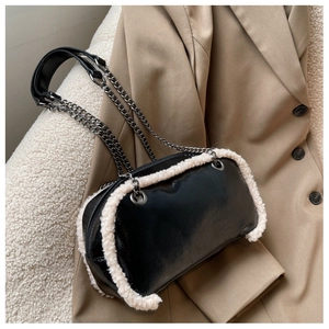Close-up of black glossy shoulder bag with white faux fur trim and silver chain strap