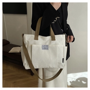 Close-up of a white corduroy tote bag with brown straps showing its texture and side pocket