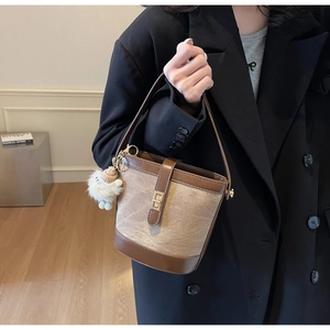 Chic canvas and leather bucket bag with gold clasp and teddy bear charm shown held