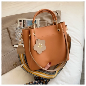 Detailansicht der braunen Beuteltasche mit Blumenanhänger und breitem Schultergurt