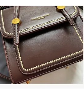 Macro detail of vintage brown leather bag featuring beige zigzag stitching and gold buttons
