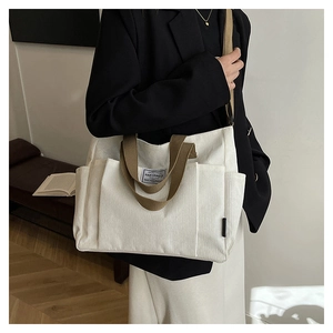Close-up of white corduroy tote bag featuring brown straps and a front pocket detail