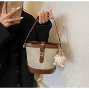 Close-up of canvas bucket bag with brown leather trim and plush doll pendant detail