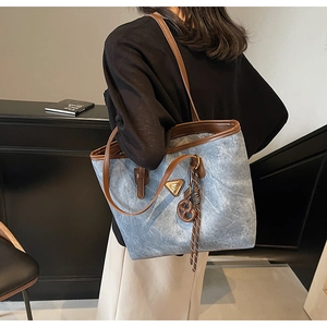 Détail du sac cabas gris-bleu avec garniture en cuir marron et badge en métal doré