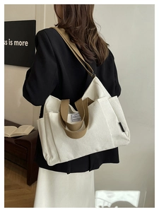 Close-up of white corduroy tote bag featuring brown straps and brand woven label detail