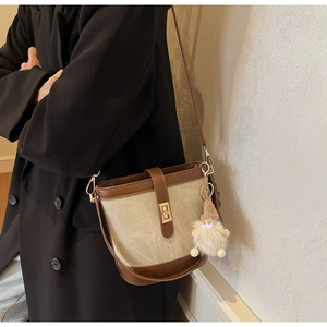 Detail of canvas bucket bag with brown leather trim, gold twist lock, and gnome charm