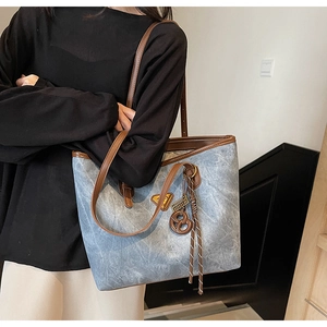 Détail du cabas en denim bleu avec lanières brunes et breloque bretzel sur modèle