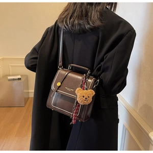 Detail of dark brown vintage leather crossbody bag with teddy bear charm and silk scarf