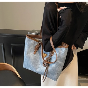 Détail du cabas en denim bleu avec garniture en cuir marron et logo en métal