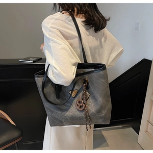 Détail du sac cabas gris aspect vieilli avec logo triangle en métal et pendentif marron