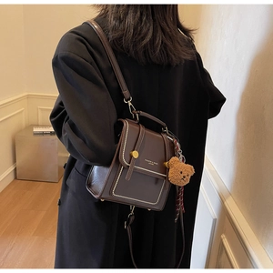 Detail of dark brown PU leather crossbody bag with a cute plush bear charm and gold buckle