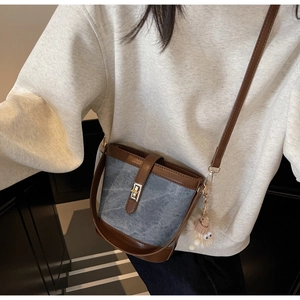 Detail view of denim and brown leather bucket bag with a cute plush charm and gold buckle