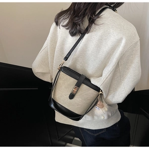 Detail view of beige bucket bag with black leather trim and golden metal turn lock