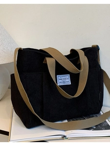 Black corduroy tote bag with khaki straps and blue brand label in a stylish lifestyle setting