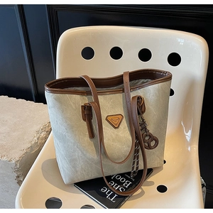 Détail d'un grand sac cabas gris avec des anses en cuir marron sur une chaise blanche