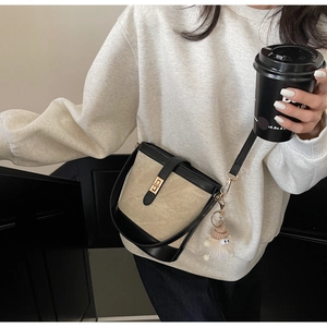 Detail of beige and black bucket bag with gold twist lock and plush charm on model