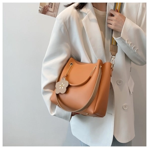 Detail der hellbraunen Beuteltasche mit breitem Webriemen und Blumenanhänger auf weißem Blazer