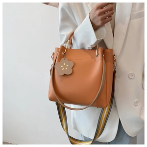 Detail der orangefarbenen Beuteltasche mit Blumenanhänger und gestreiftem Schultergurt