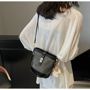 Detail of black leather bucket bag with gold clasp and white plush sheep pendant