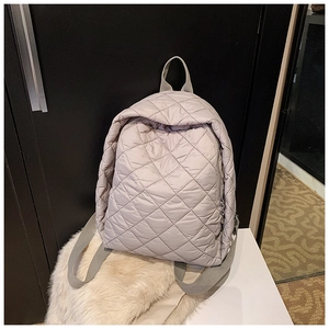 Détail d'un sac à dos matelassé gris clair avec coutures en losange et zip métallique