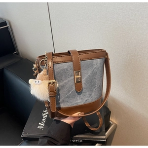Detail of denim and leather bucket bag with gold lock and plush charm accessory