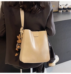 Detail of minimalist beige bucket bag with rabbit charm and wide strap on model