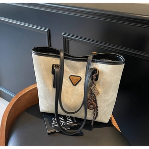 Détail du grand sac cabas gris avec logo triangulaire et pendentif tressé sur une chaise