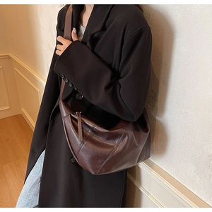 Brown leather crescent bag with slouchy texture worn over a dark oversized blazer