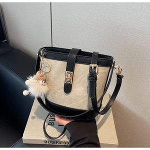 Detail of canvas bucket bag with black leather trim, golden twist lock and plush charm